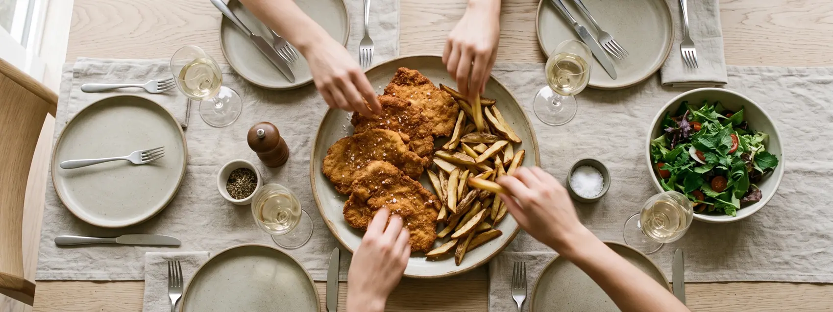 Mesa servida con milanesas y papas fritas, varias manos sirviéndose